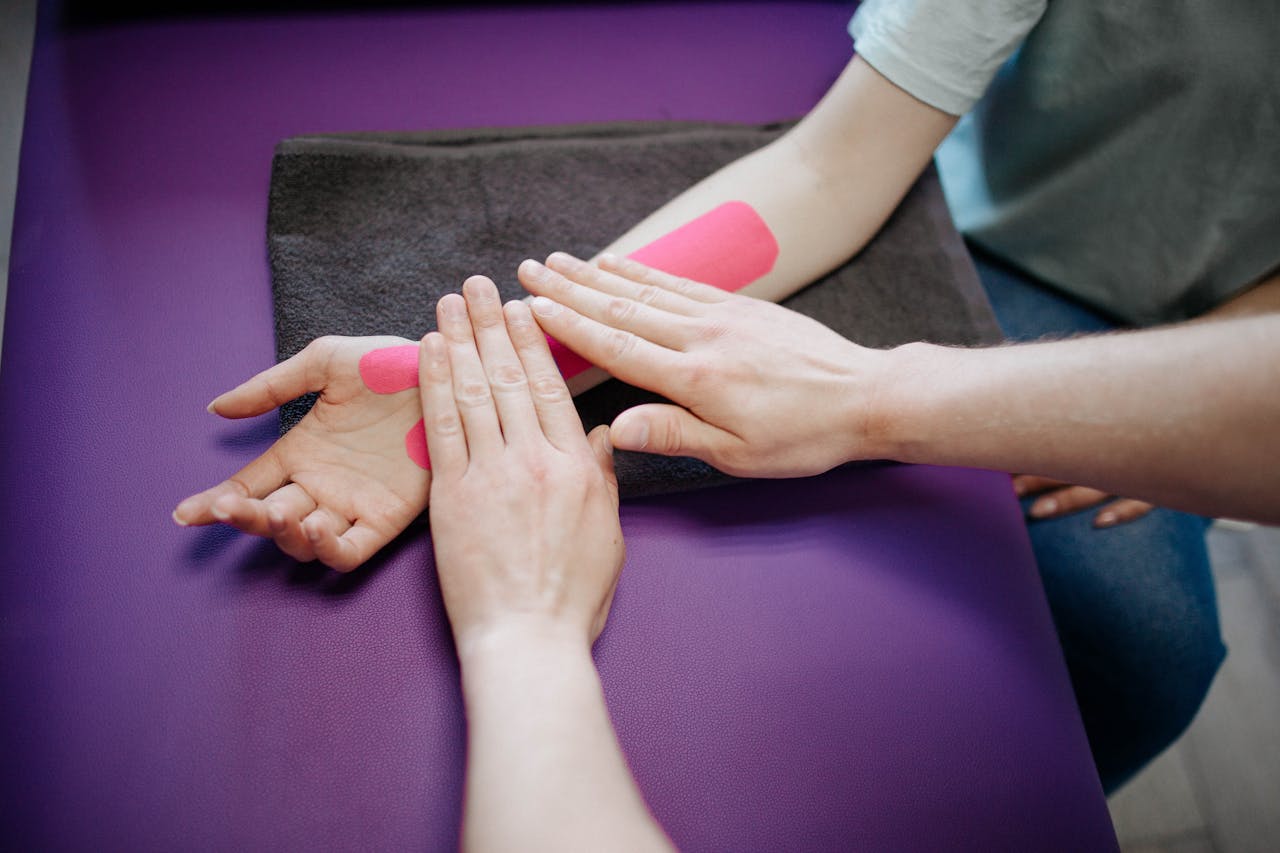 Close-up of hands applying pink kinesiology tape during a relaxing arm massage.